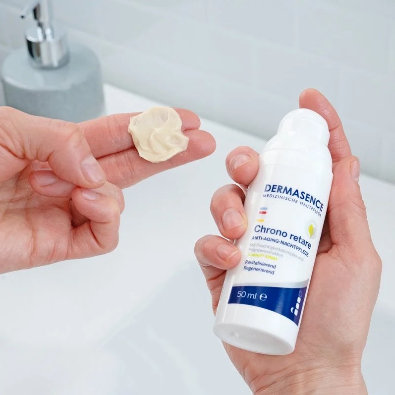 Beige rijke balm van revitaliserende nachtcreme op twee vingers met de verpakking in de andere hand.