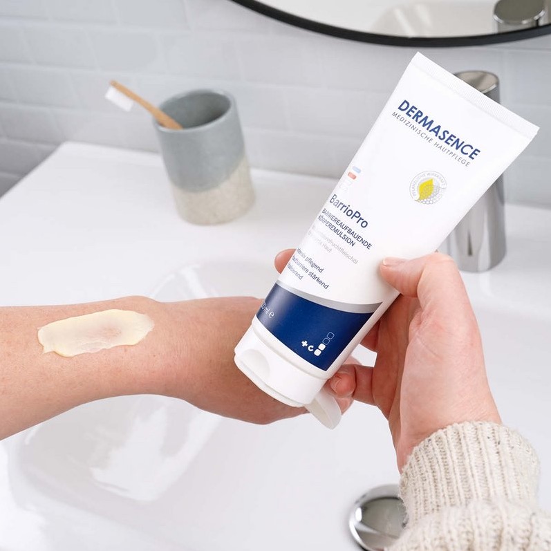 DERMASENCE BarrioPro tube wordt aangebracht op een geïrriteerde huidplek op de arm in een badkamer.