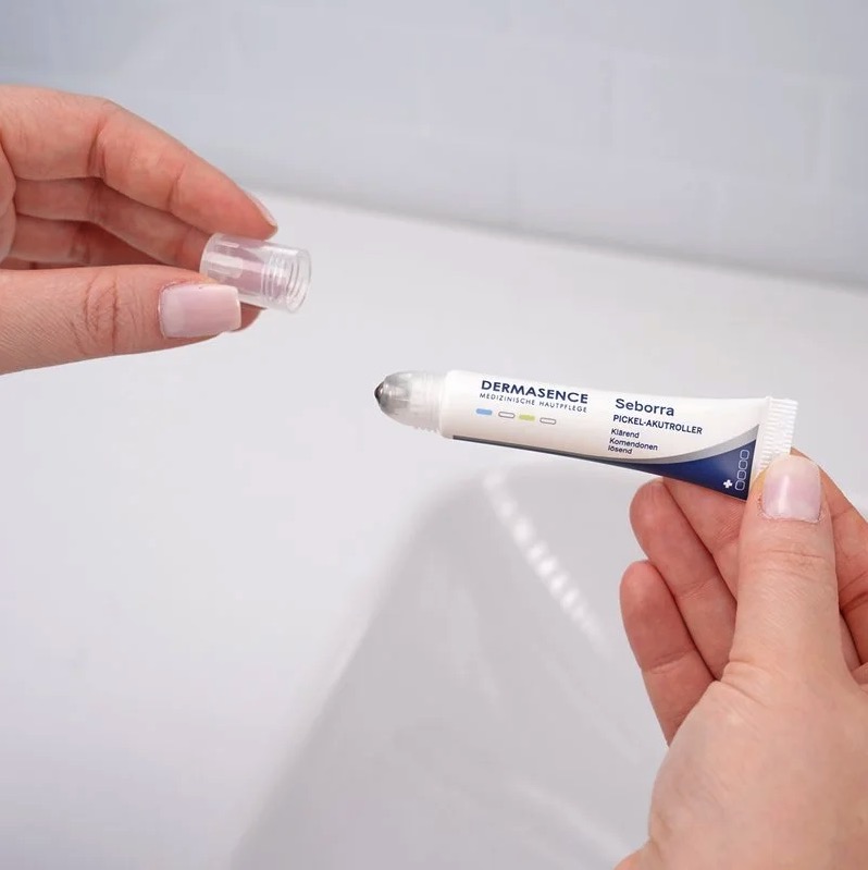 Boven een witte wasbak laat een paar handen de pimple relief roll-on zien met de dop eraf
