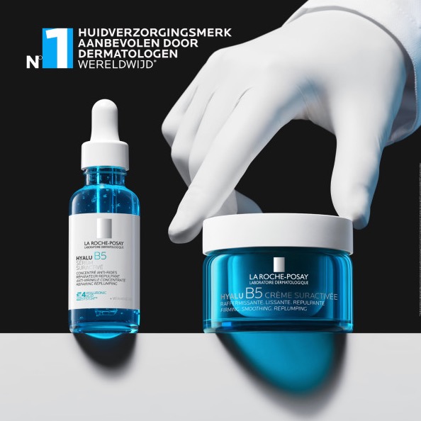 Een blauwe fles met pipet en een glazen pot La Roche-Posay Hyalu B5 staan naast elkaar op een witte ondergrond. Een hand met een witte handschoen raakt de crèmepot aan. Bovenaan staat: “Nr. 1 huidverzorgingsmerk aanbevolen door dermatologen wereldwijd.”