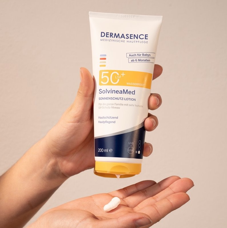 Hand met een tube Dermasence SolvineaMed SPF 50+ zonnebrand en een beetje witte crème in de andere hand.