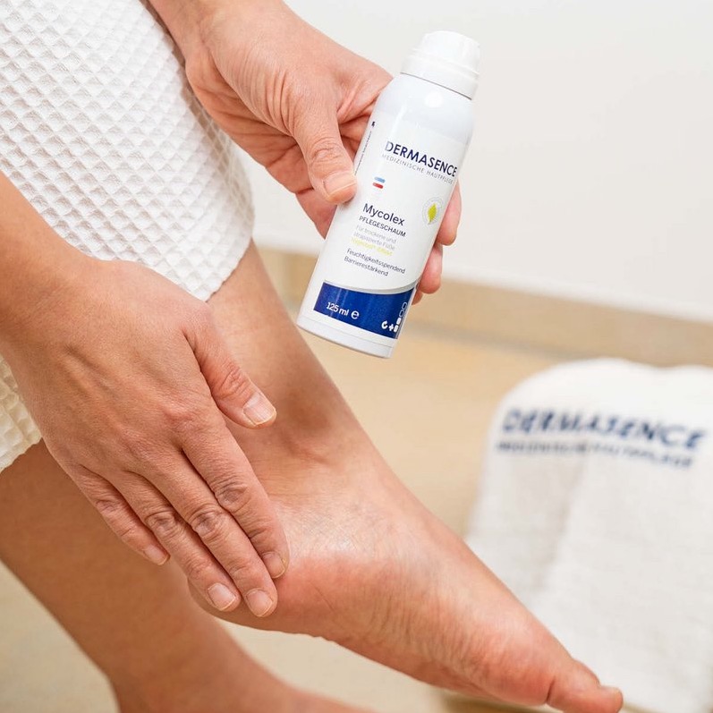 Persoon brengt DERMASENCE Mycolex verzorgingsschuim aan op de hiel en enkel van de voet.